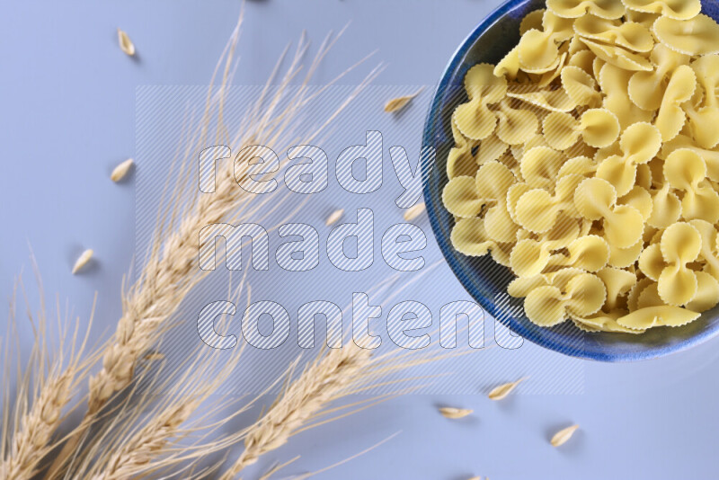 Raw pasta with wheat stalks on light blue background