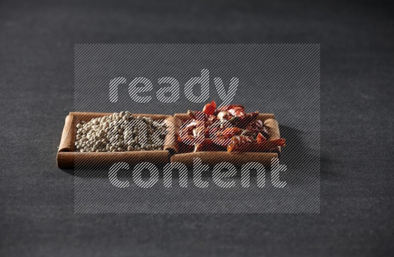 مربعان من أعواد القرفة ممتلئان بالفلفل الحار المجفف وحبوب الفلفل الأبيض علي خلفية سوداء