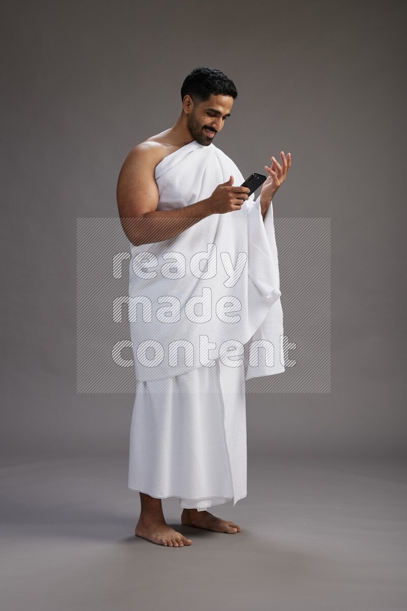 A man wearing Ehram Standing texting on phone on gray background