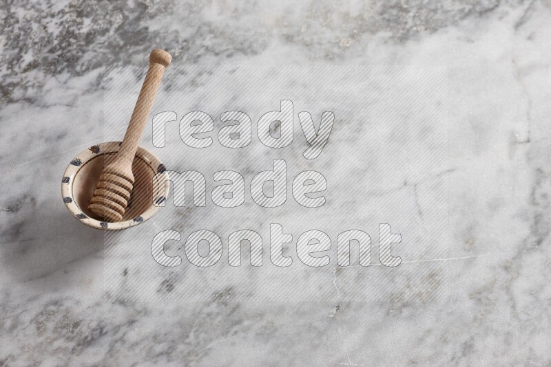 Decorative pottery bowl with wooden honey dipper in it on grey marble background