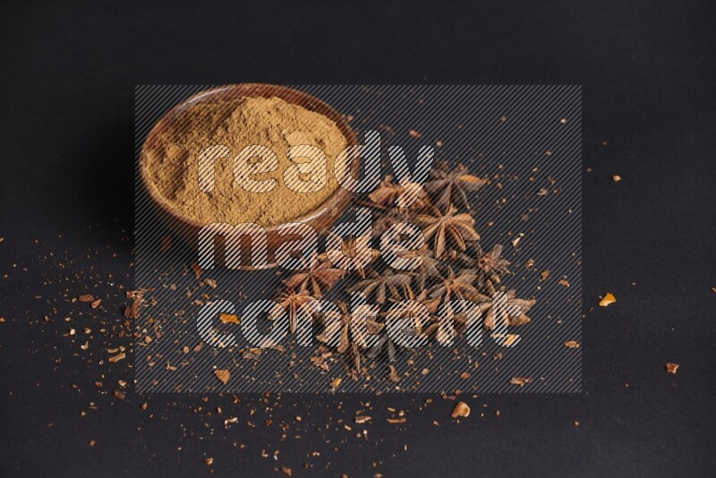 Star Anise powder in a wooden bowl with star anise beside it on a black background