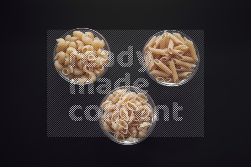 Different pasta types in glass bowls on black background