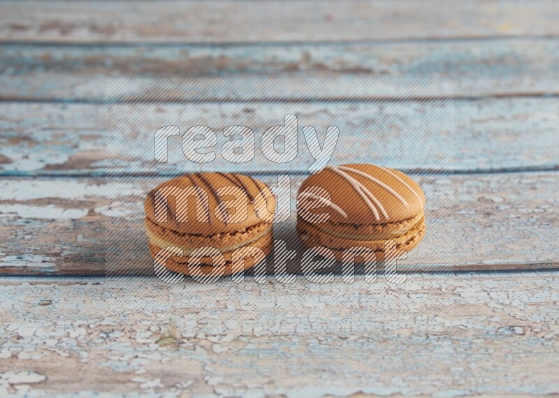 45º Shot of of two assorted Brown Irish Cream, and light brown Almond Cream macarons next to each other on light blue background
