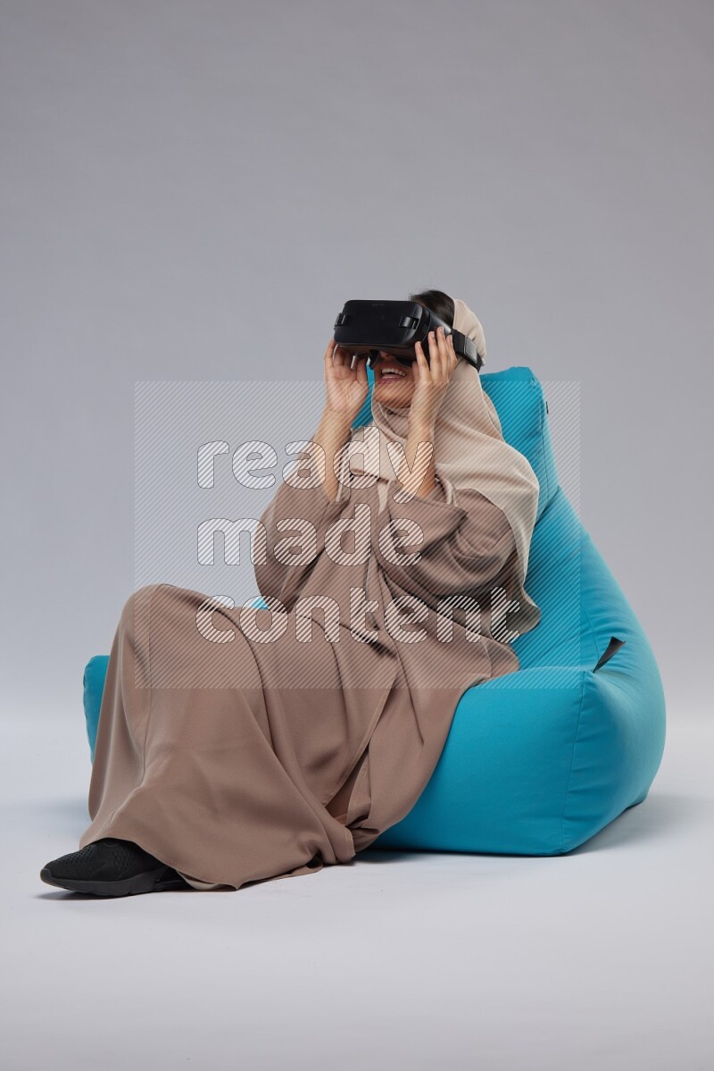 A Saudi woman sitting on a blue beanbag and gaming with VR