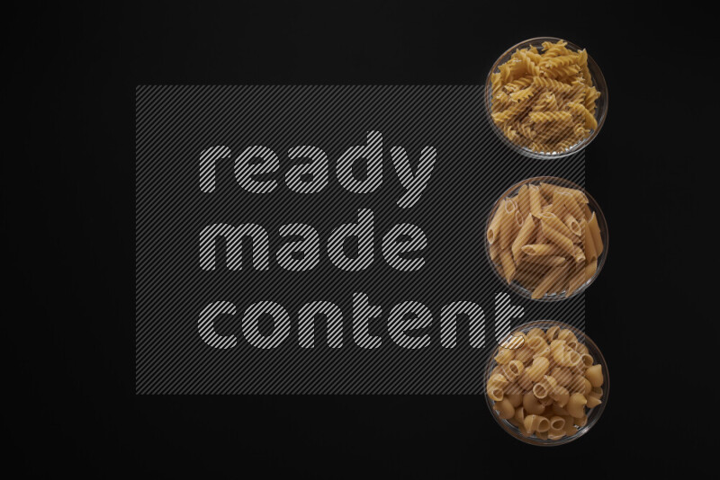 Different pasta types in 3 glass bowls on black background