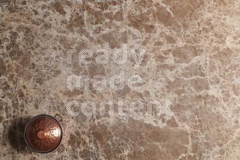 A small copper pot on beige marble background