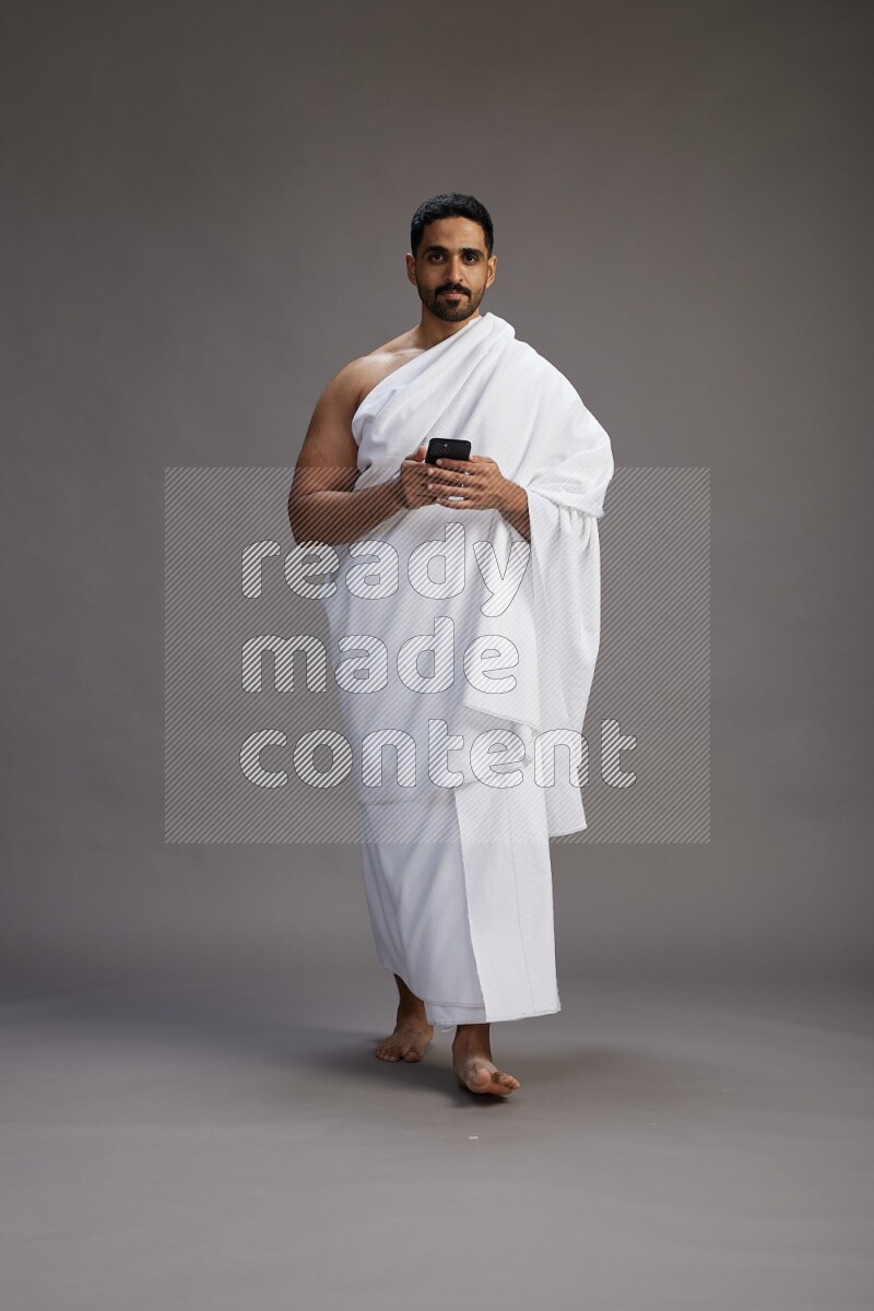 A man wearing Ehram Standing texting on phone on gray background