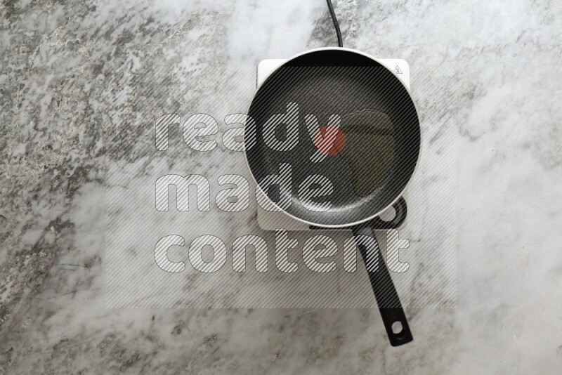 Frying pan on single electric stove on grey marble background