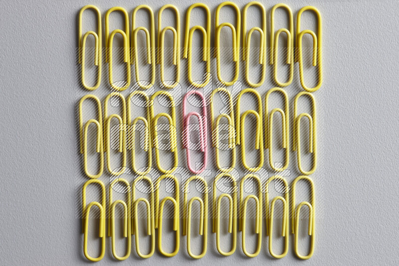 A bunch of yellow paper clips with a different colored paper clip in the center on grey background