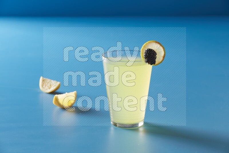 glass of lemon juice with lemon slice and berry on blue background