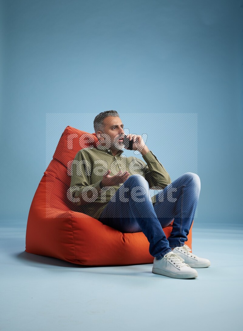 A man sitting on an orange beanbag and talking on the phone