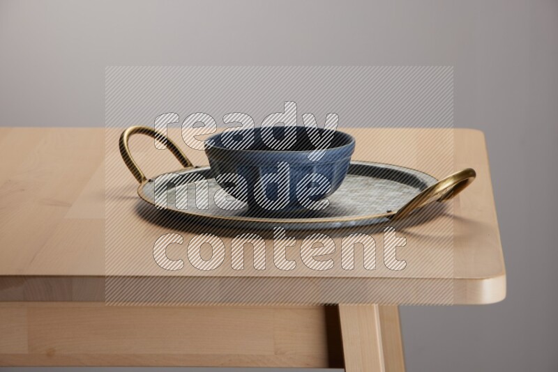 blue bowl placed on a rounded stainless steel metal tray with golden handels on the edge of wooden table