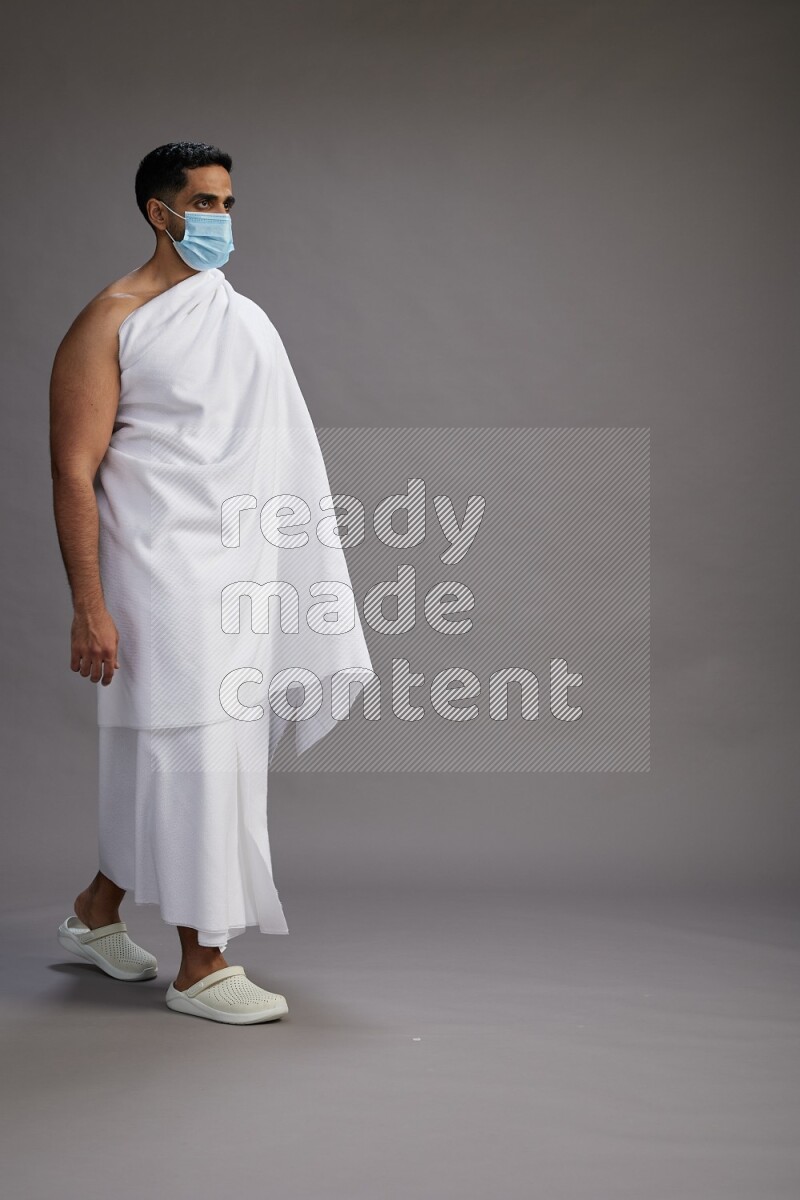 A man wearing Ehram with face mask Standing Interacting with the camera on gray background