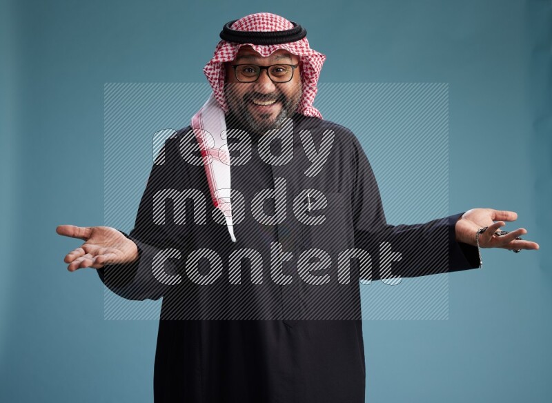 Saudi Man with shimag Standing Interacting with the camera on blue background