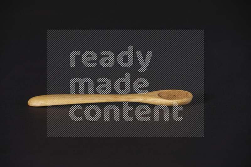 Cinnamon powder in a wooden spoon on a black background