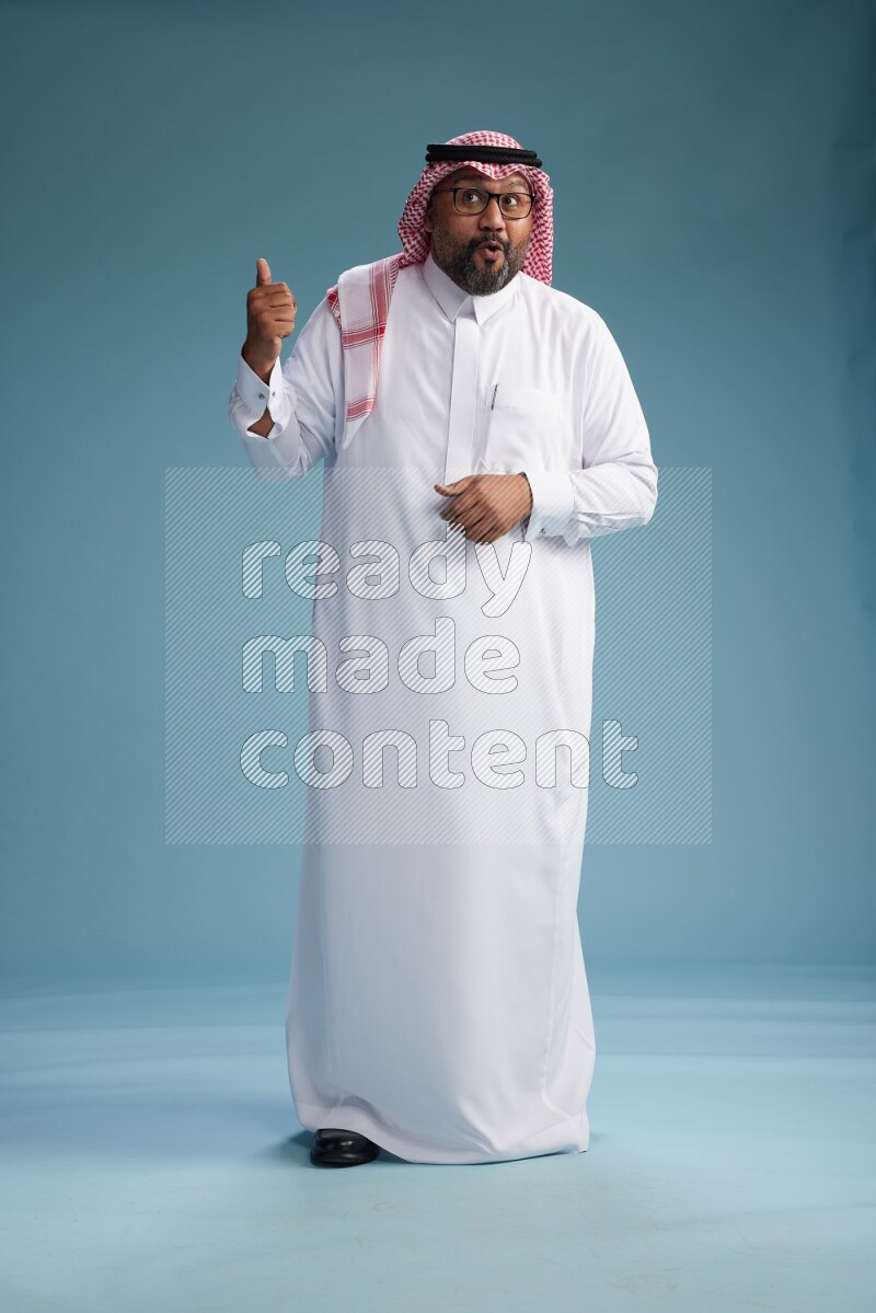 Saudi Man with shimag Standing Interacting with the camera on blue background