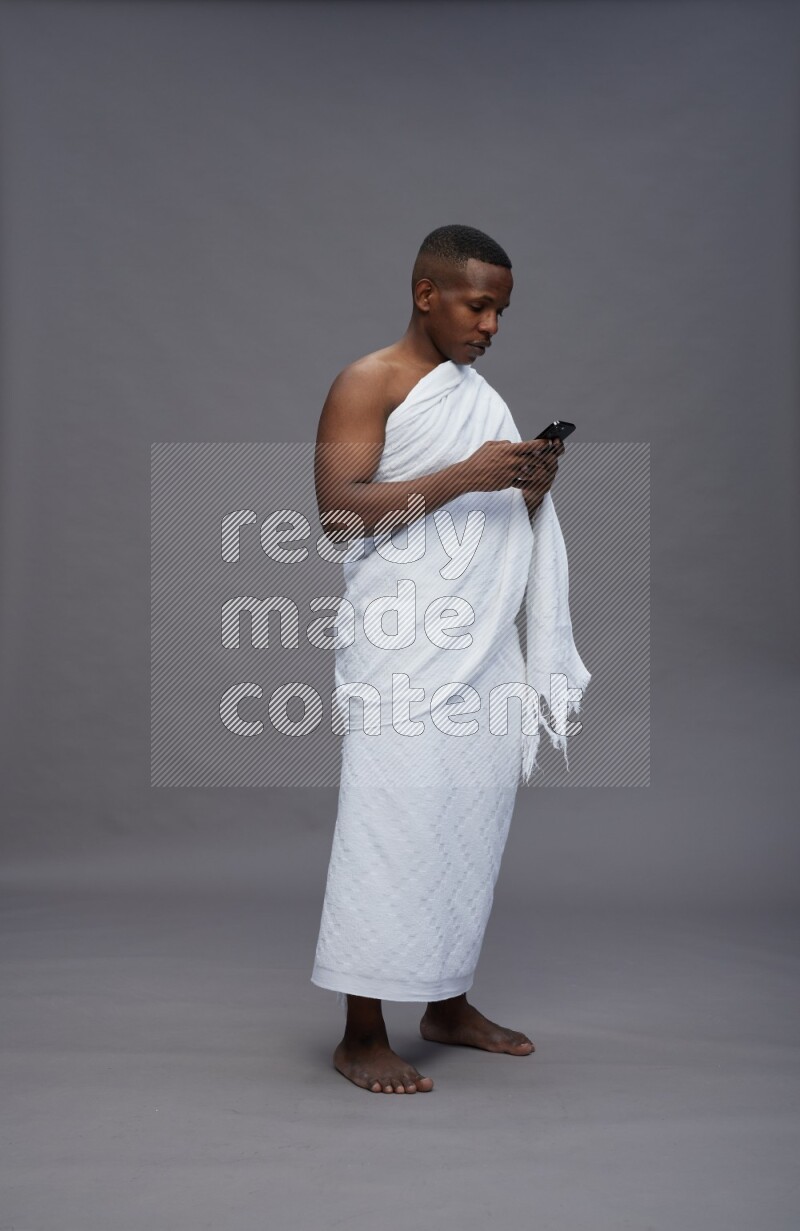 A man wearing Ehram Standing texting on phone on gray background