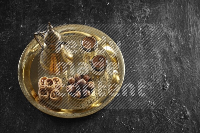 Oriental sweets with dates and a drink on a metal tray in a dark setup