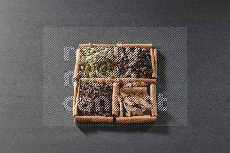 4 مربعات من عيدان القرفة ممتلئة بحبوب القهوة وقطع القرفة والقرنفل وحبوب الهيل على أرضية سوداء