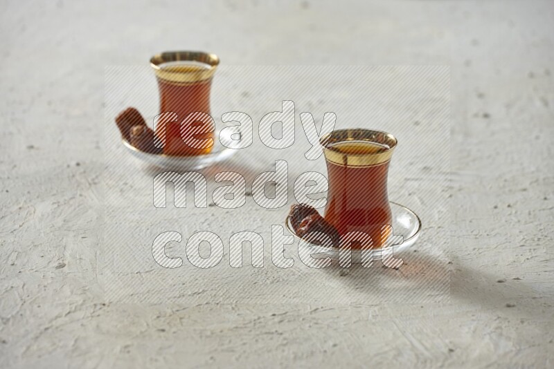 A tea glass cup with dates and coffee on textured white background