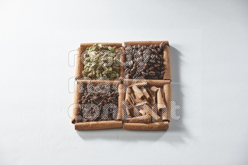 4 مربعات من أعواد القرفة ممتلئة بحبوب القهوة والقرفة والقرنفل والهيل على أرضية بيضاء