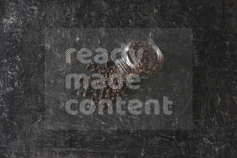 وعاء زجاجي للبهارات مقلوب ممتلئ بالقرنفل والقرنفل سقط منه على أرضية سوداء