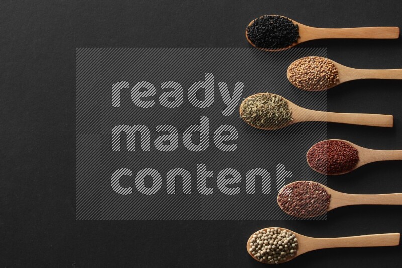 wooden spoons filled with white peppers, mustard seeds, black seeds, garden cress, cumin and flax on black flooring