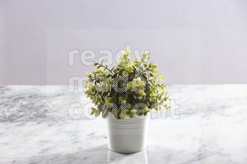 Green artificial plant in white pot on light grey marble background