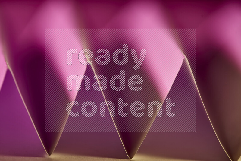 A close-up abstract image showing sharp geometric paper folds in pink gradients and warm tones