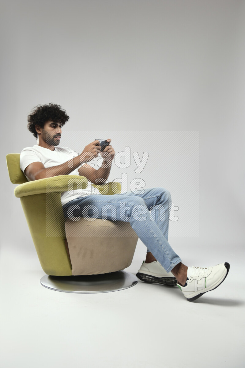 A man wearing casual sitting on a chair gaming on the phone on white background