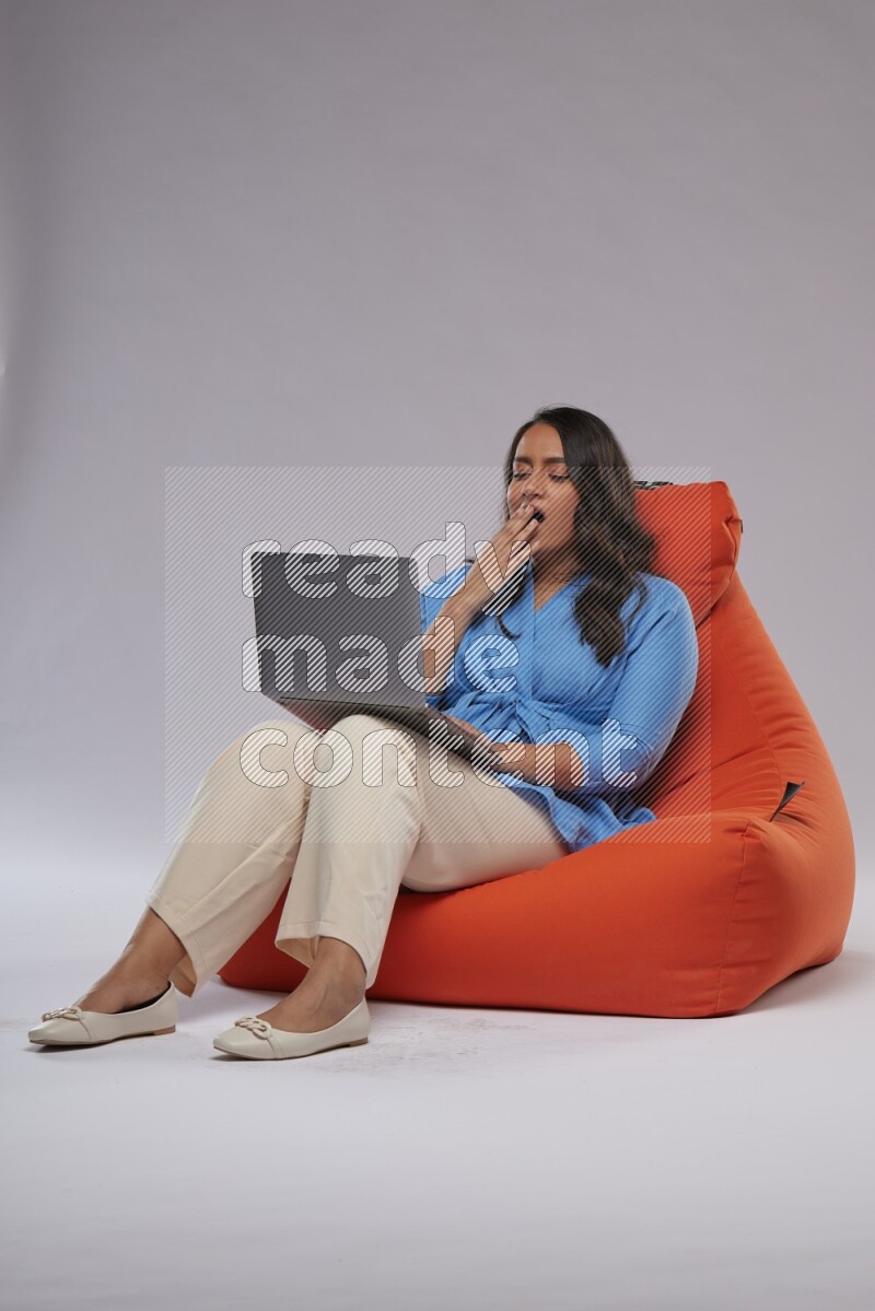 A woman sitting on an orange beanbag and working on laptop
