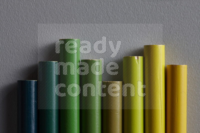 A collection of colored pencils arranged showcasing a gradient of green hues on grey background