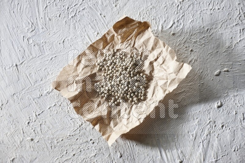 White pepper beads in a crumpled piece of paper on textured white flooring
