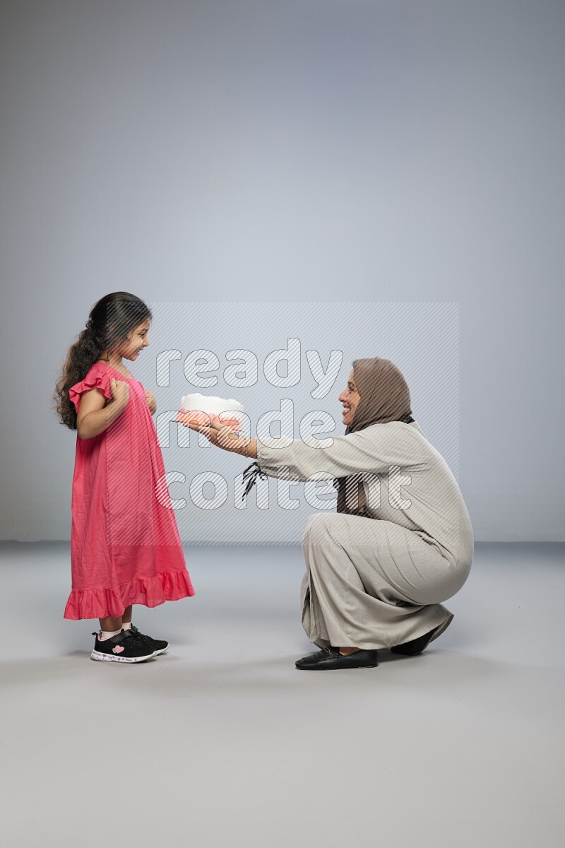A mother giving a cake to her daughter on gray background
