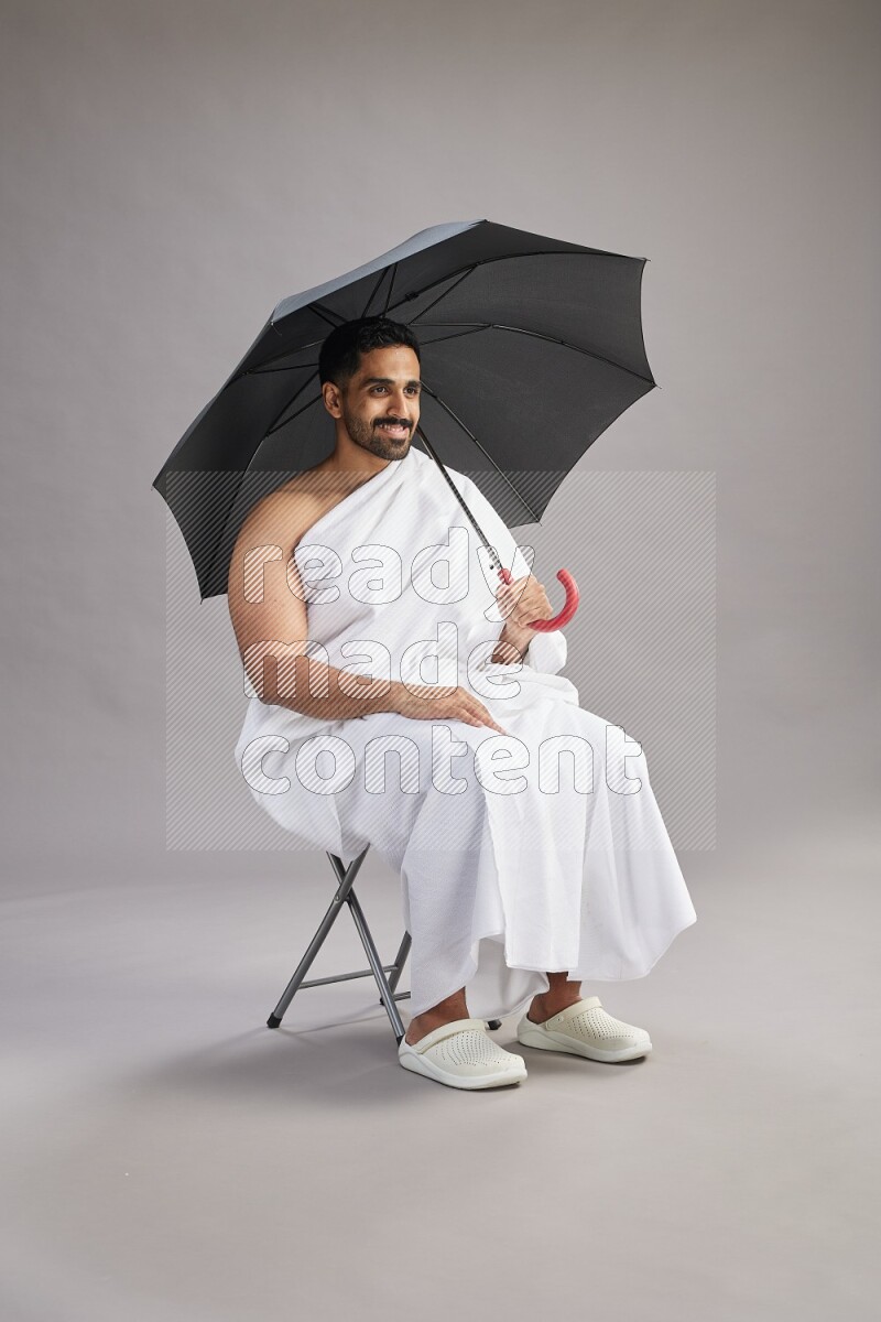 A man wearing Ehram with face mask Standing holding umbrella on gray background