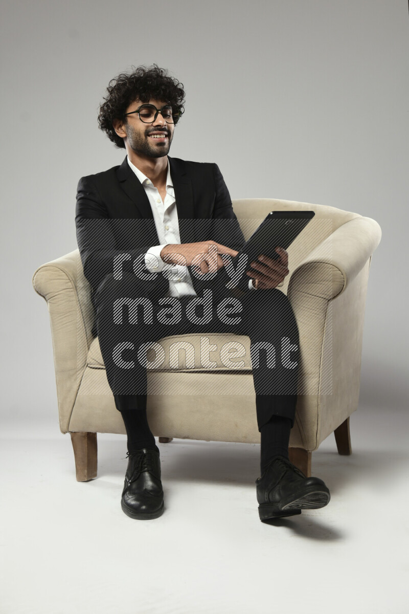 رجل يرتدي ملابس رسمية يجلس علي كرسي و يتصفح تابلت علي خلفية بيضاء