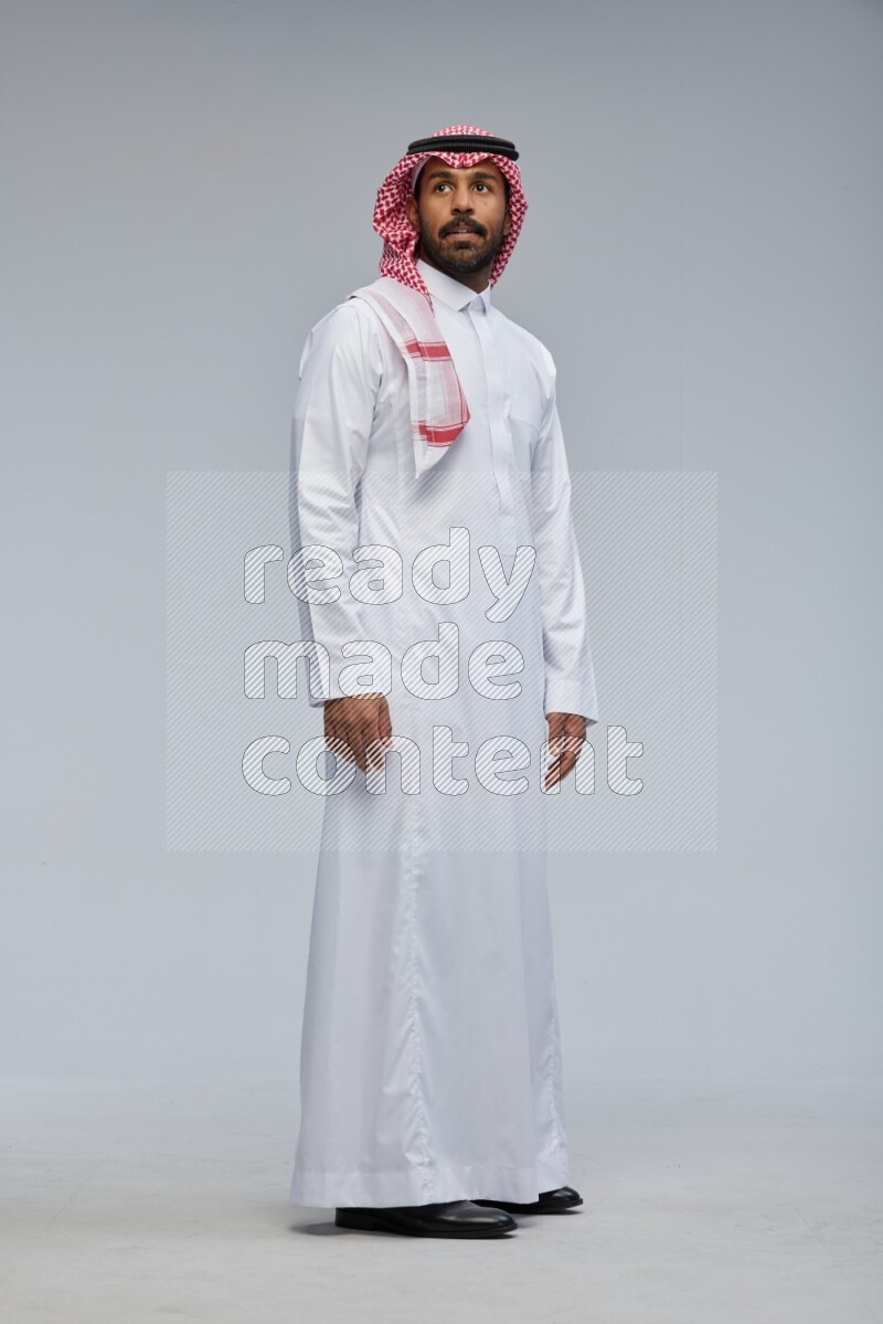 Saudi man Wearing Thob and shomag standing interacting with the camera on Gray background