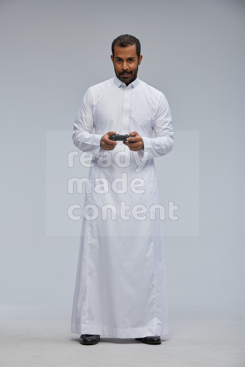 Saudi man Wearing thob standing holding joystick on Gray background
