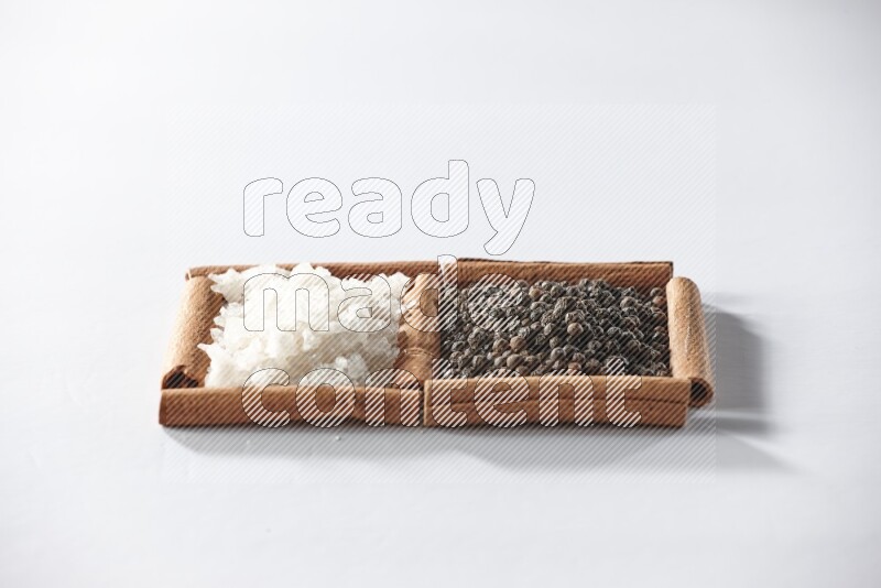 2 squares of cinnamon sticks full of black pepper and white salt on white flooring