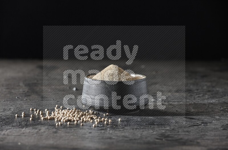 وعاء فخار أسود مملوء ببودرة الفلفل الأبيض مع حبات الفلفل الأبيض على أرضية سوداء