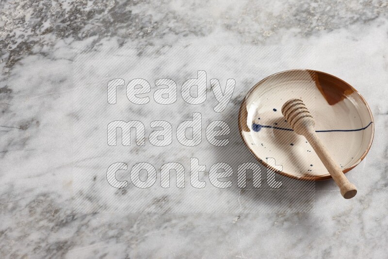 Multicolored pottery plate with wooden honey dipper in it on grey marble background