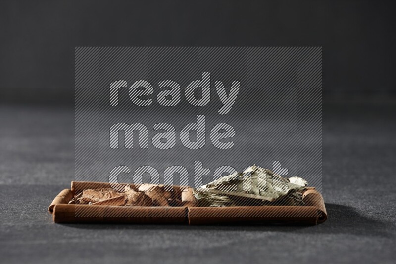 مربعان من أعواد القرفة ممتلئان بقطع من القرفة وأوراق الغار علي خلفية سوداء