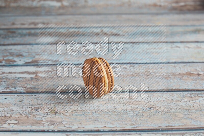 45º Shot of light brown Almond Cream macaron on light blue wooden background