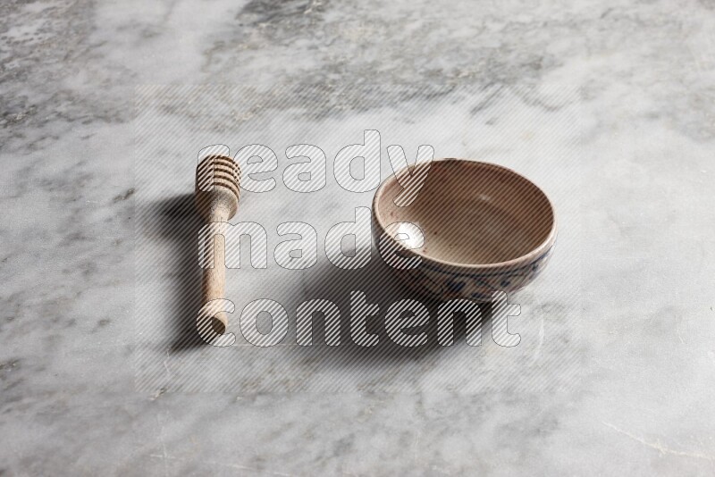 Decorative pottery bowl with wooden honey dipper on the side on grey marble background