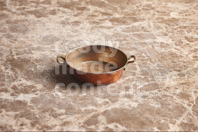 A small copper pan on beige marble background