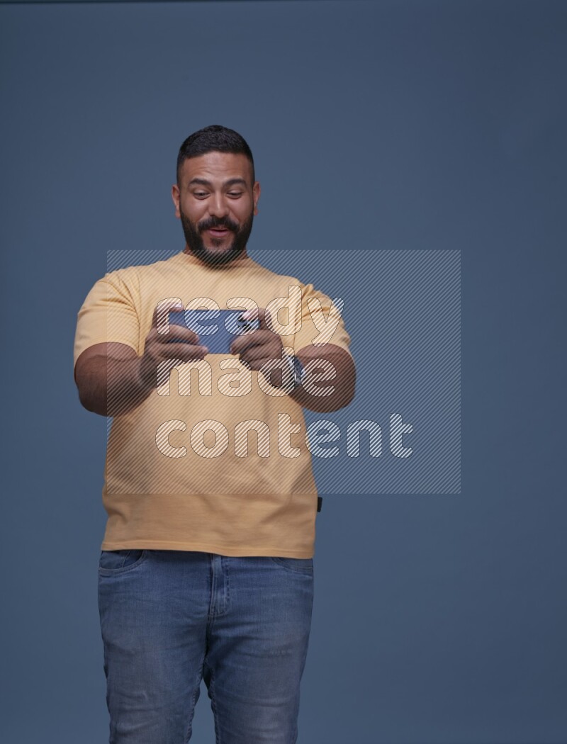 A man Playing Games on Smartphone on Blue Background wearing Orange T-shirt
