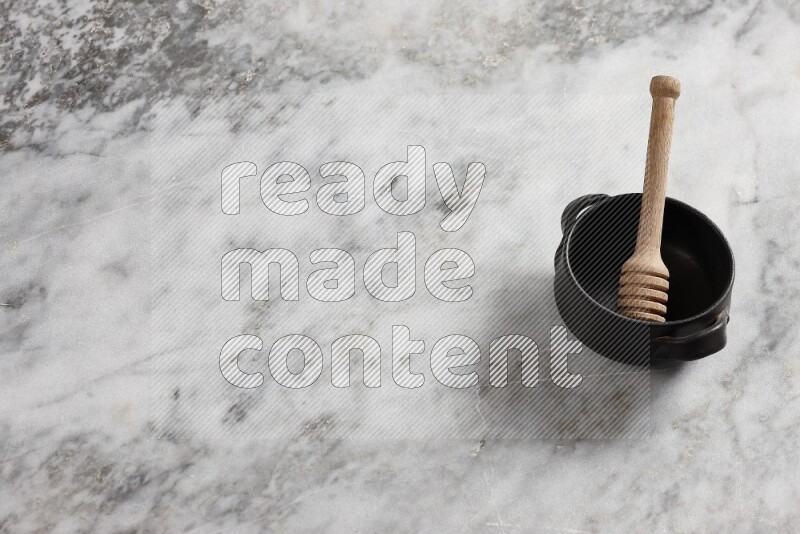 Black pottery bowl with wooden honey dipper in it on grey marble background