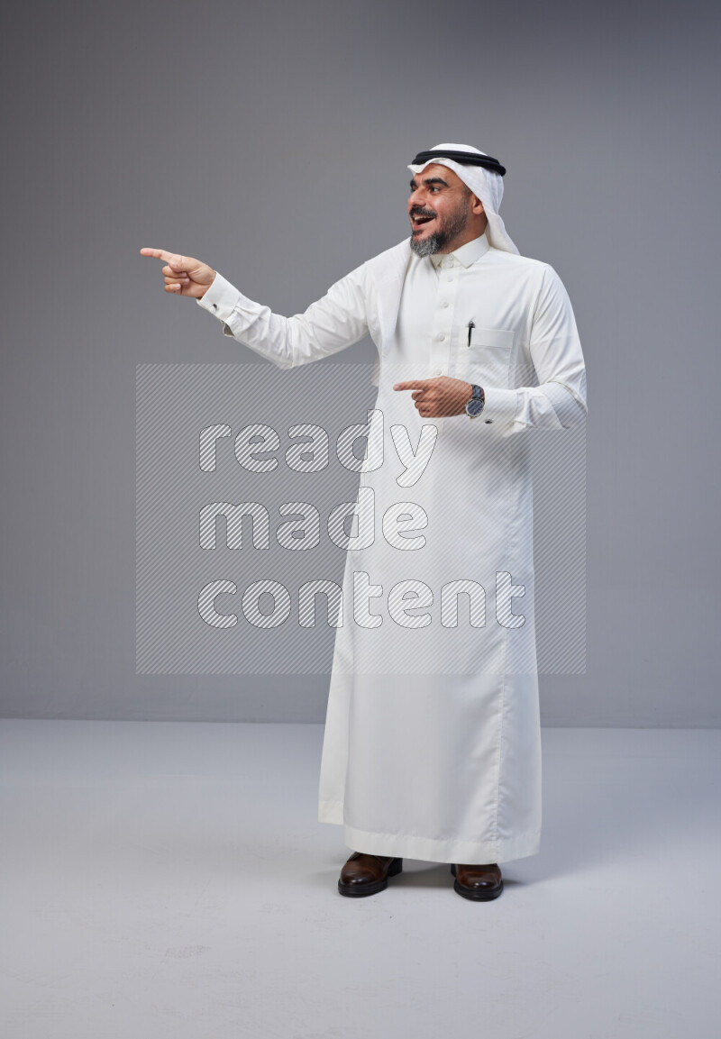Saudi man Wearing Thob and white Shomag standing interacting with the camera on Gray background