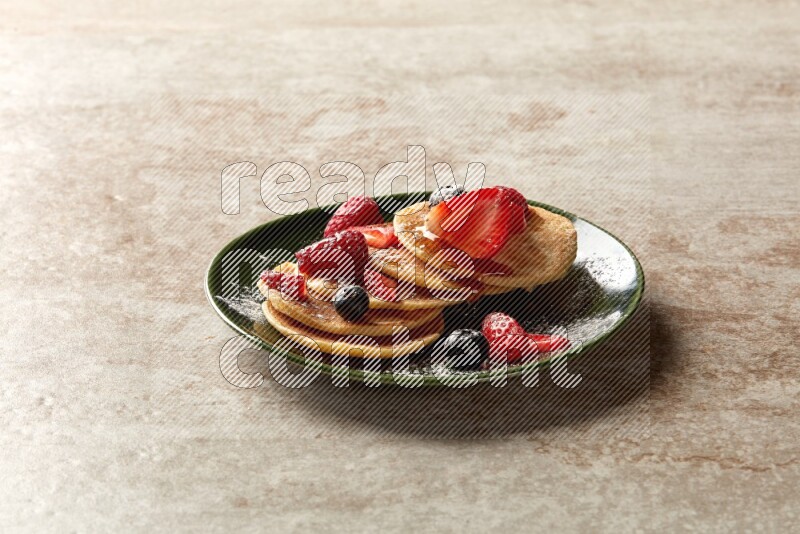Five stacked mixed berries mini pancakes in a green plate on beige background