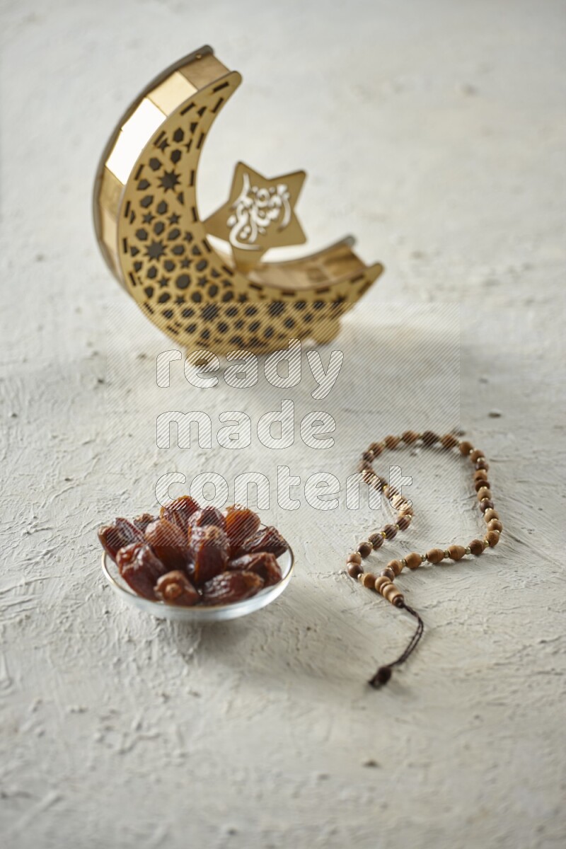 A wooden golden crescent lantern with different drinks, dates, nuts, prayer beads and quran on white background